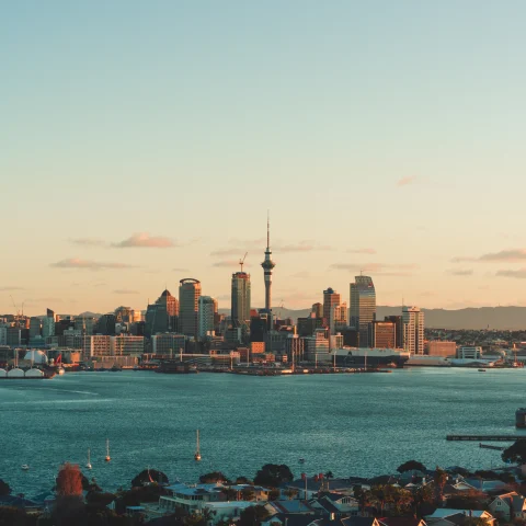A city view of Auckland, New Zealand at sunset overlooking a blue lake.