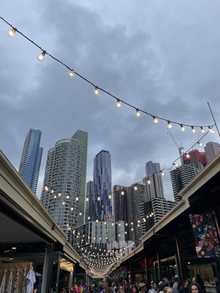 A low-angled view of string lights and tall skyscrapers in Melbourne with many people walking below