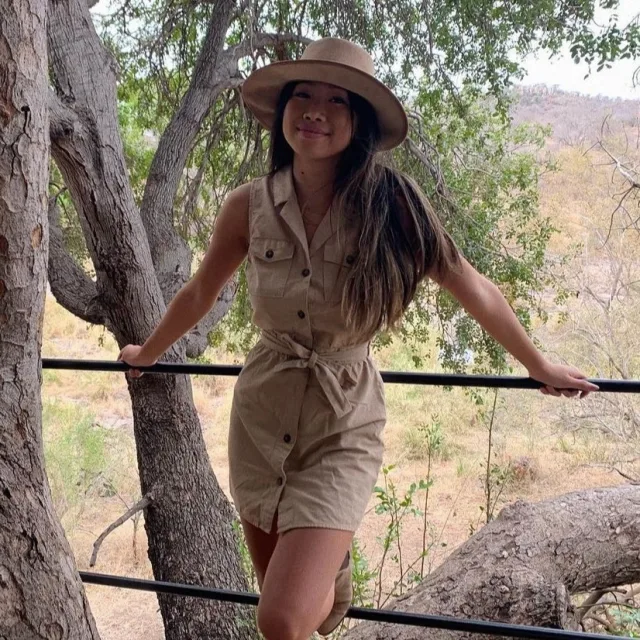 Travel Advisor Kristy Thai wears a camel colored dress and hat in a safari scene 