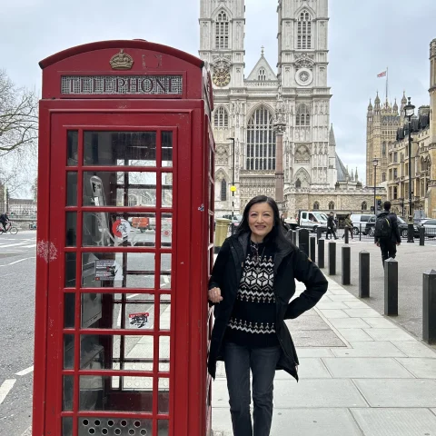 An image of a woman posing next to a red telephone booth in London with a large stone cathedral in the background. 