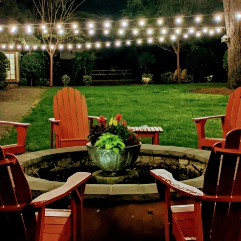 chairs around a fire pit with string lights