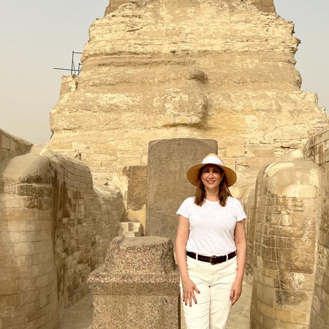 Fora travel agent Gia Crecelius wears white hat and stands in front of historical landmark
