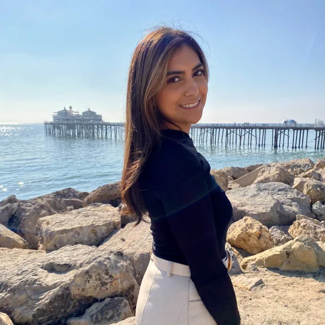 Travel Advisor Ilissa Valenciana in a black shirt and white jeans standing on rocks in front of a pier.