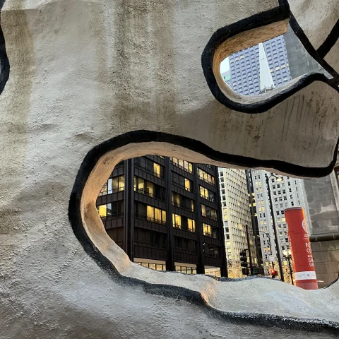 a city seen through an abstract stone-like sculpture 