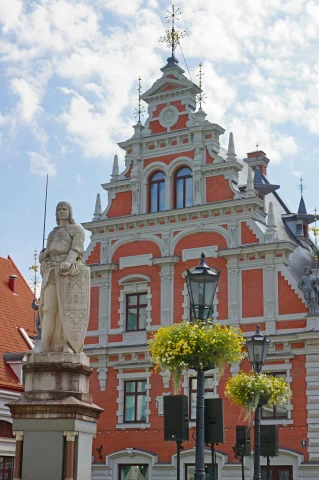 A beautiful orange and white building with a statue and street lamps in front of it on a cloudy and blue sky day.  