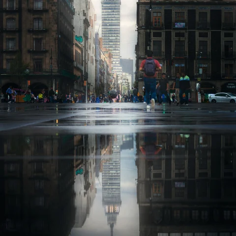 rainy day in a city, a tall building reflects in the puddle in an open plaza