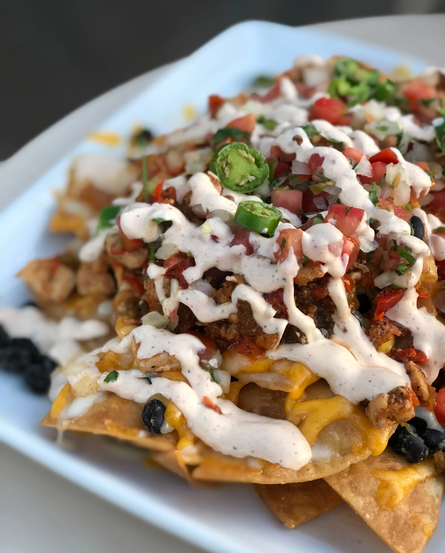 A bowl of nachos with cheese, meat and vegetables. 