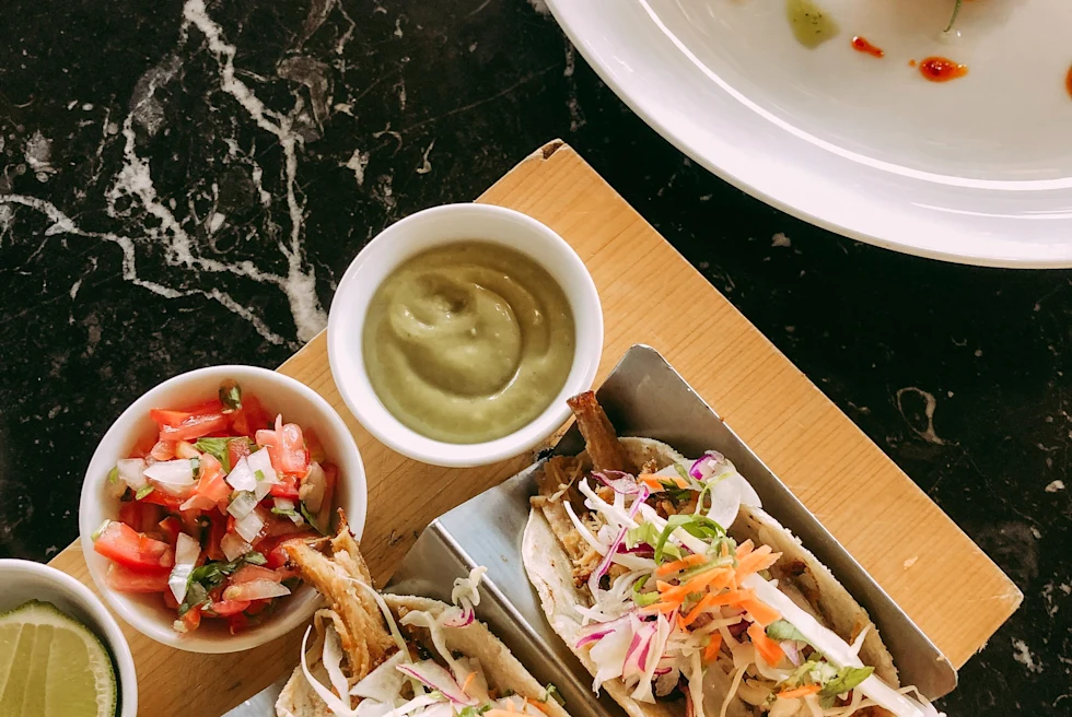 tacos on a brown cutting board next to a white plate