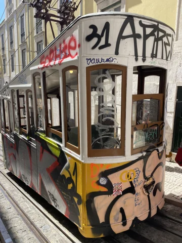 A picture of a multi-colored tram on the road during the daytime covered in street art.