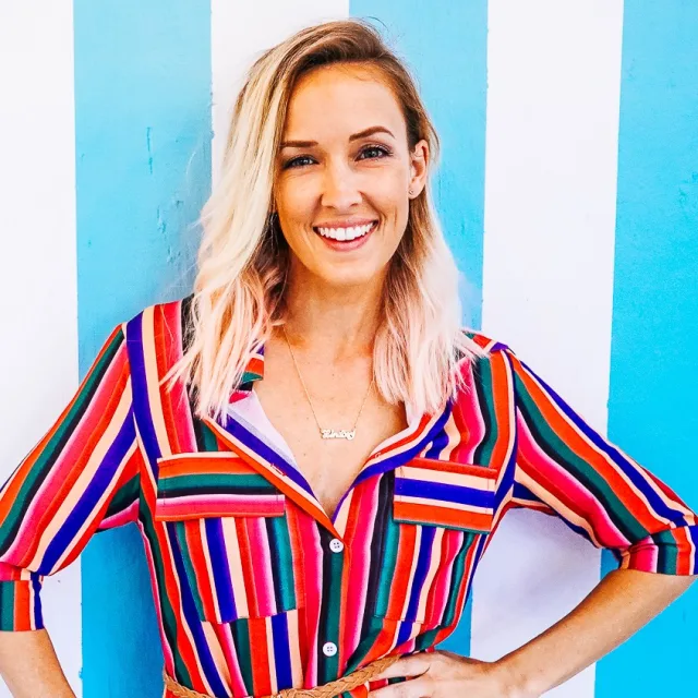 Travel Advisor Lindsey Kirkendall wears a multi colored striped blouse and poses in front of a blue and white striped wall