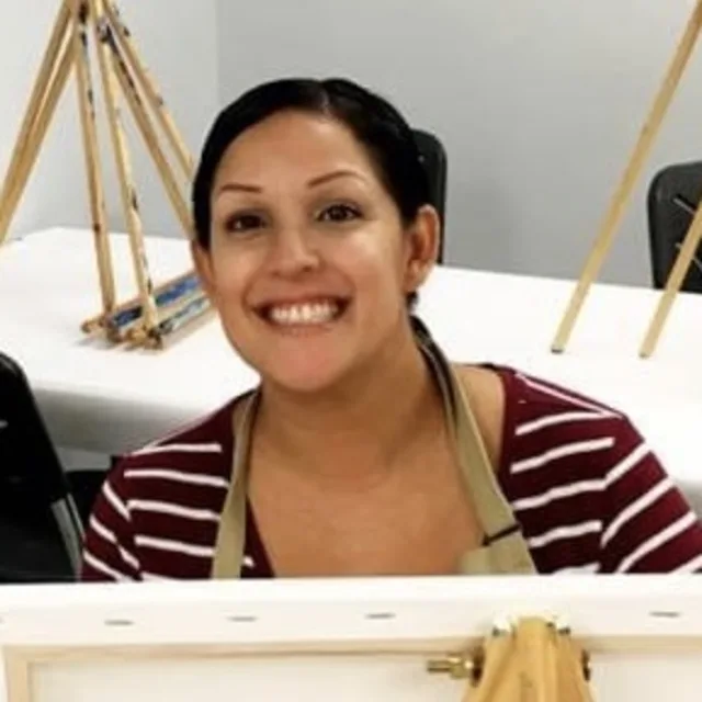 Travel advisor Anna Richards with black hair in a striped shirt painting a canvas
