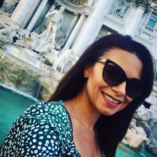 Travel Advisor Tiffany Belay poses in front of an fountain with sunglasses and a green polka dotted top