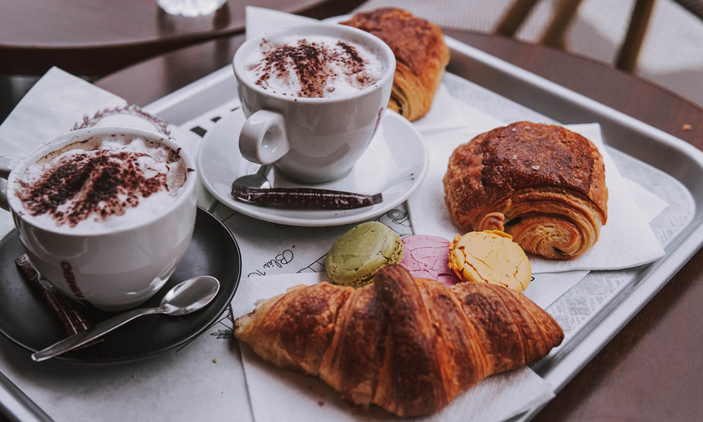 golden croissant and pain au chocolat coffee with cinnamon in white mug with metal spoon on tray in Paris France