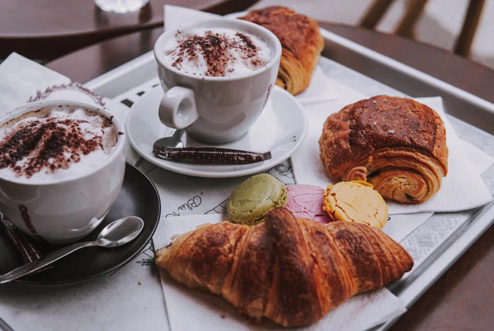 golden croissant and pain au chocolat coffee with cinnamon in white mug with metal spoon on tray in Paris France