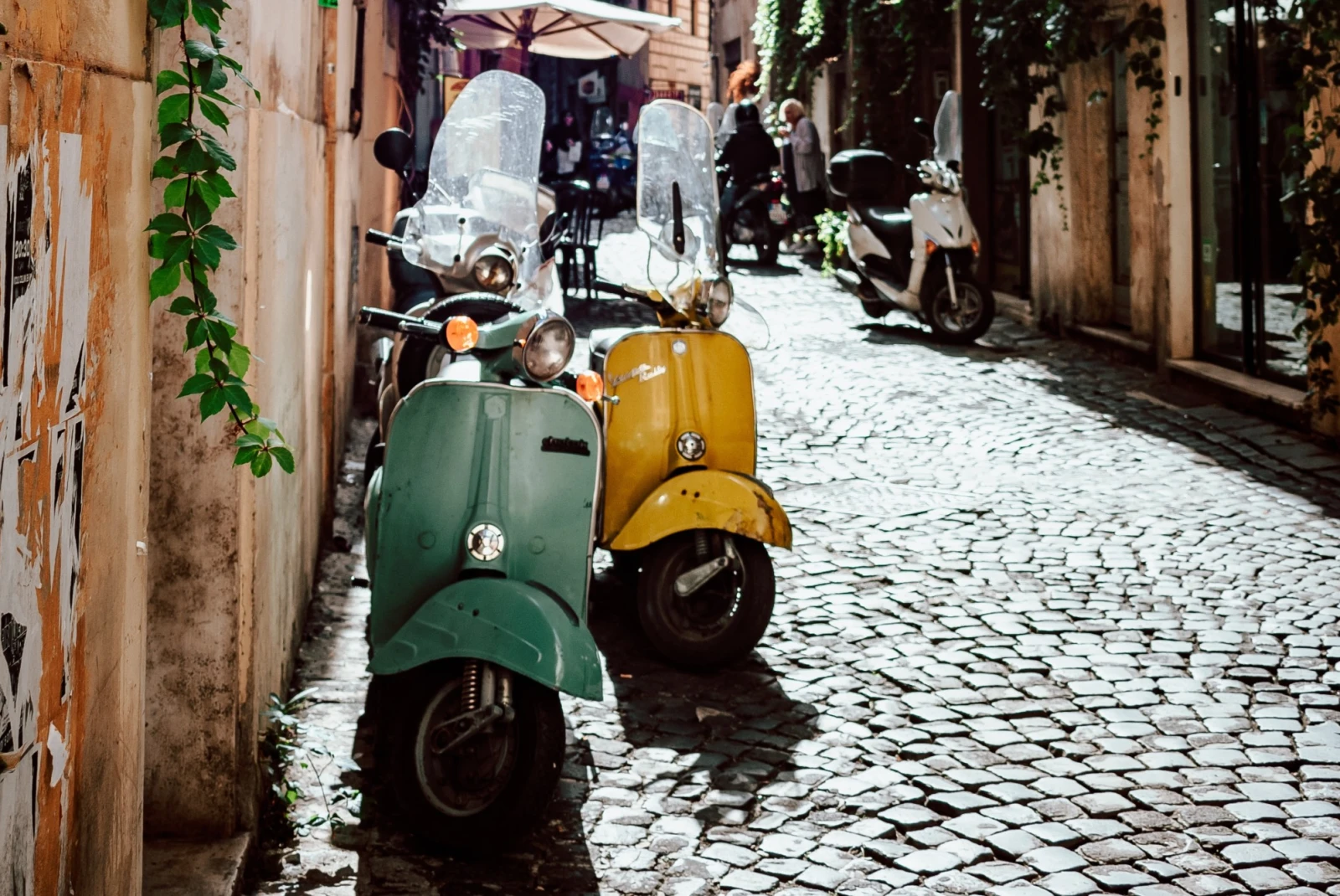 yellow and turquoise vespas side-by-side in a charming, sun-lit alley