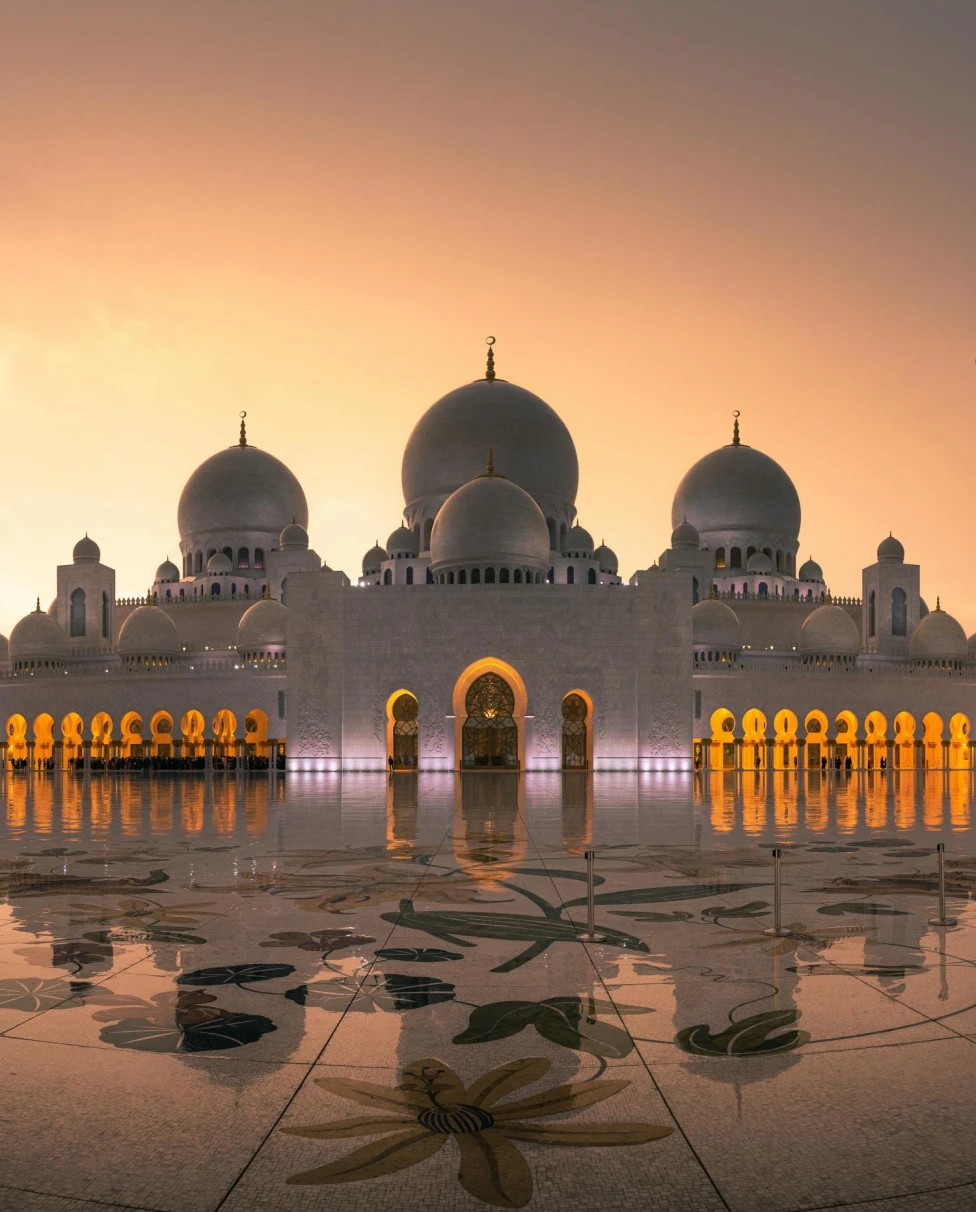 Sheikh Zayed Mosque in Abu Dhabi glowing white and gold during sunset.