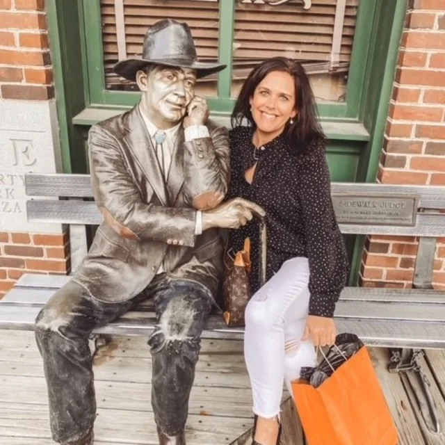 Travel Advisor Heather Lewis with a black shirt, white pants and an orange bag with a statue.