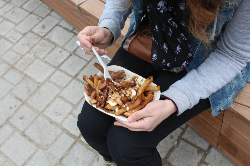 A girl eating poutine in her lap. 