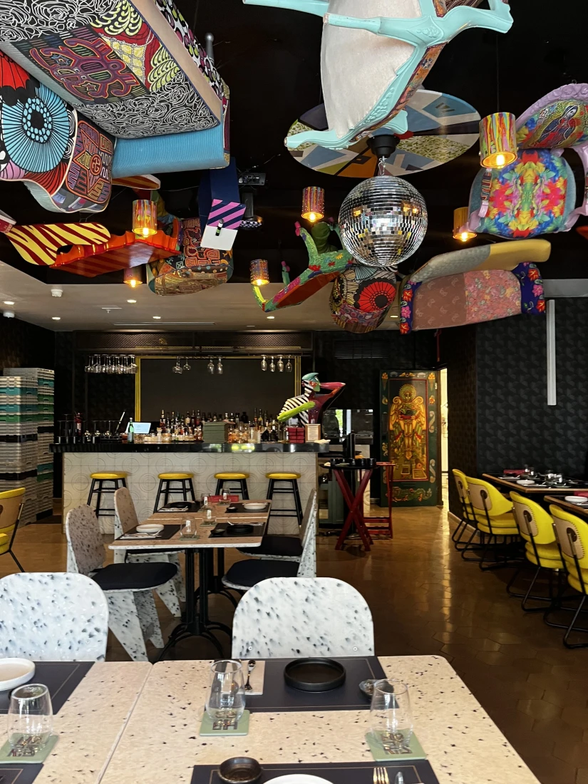 A view of a restaurant interior with seating, tables, a bar in the background and colorful decorations with a disco ball hanging from the ceiling. 