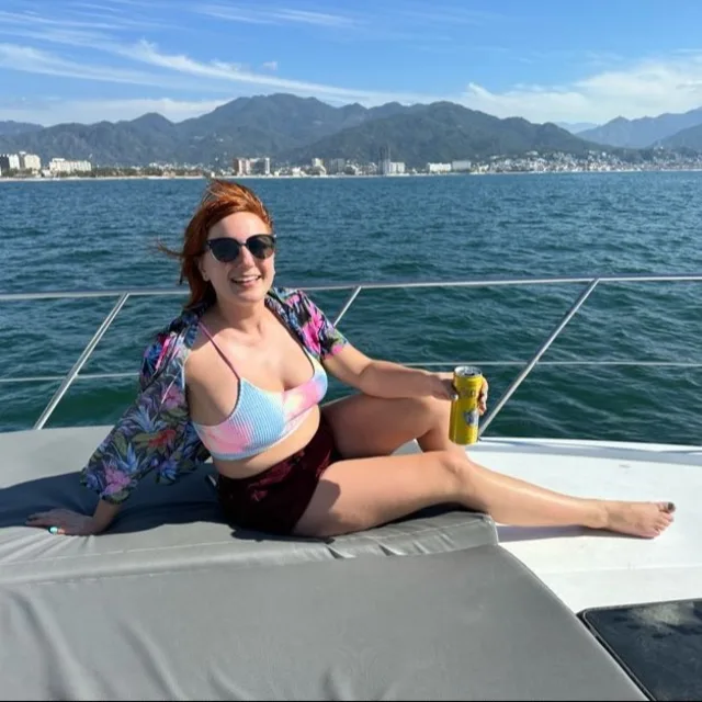 Jacqui on a boat wearing a colorful swimsuit with water and a mountain in the background
