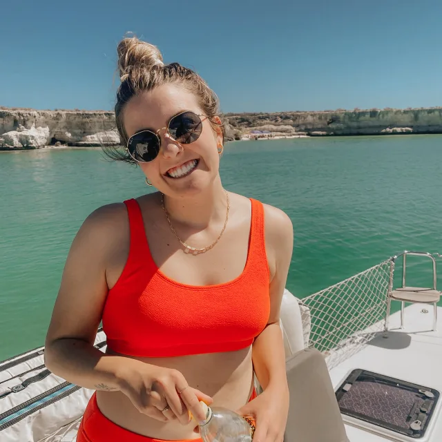 Emily Wright in an orange swimsuit holding a bottle of water on a yacht.
