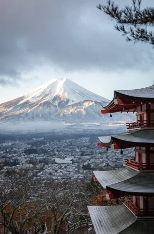 A view of an ancient red temple and Mount Fuji in the background. 