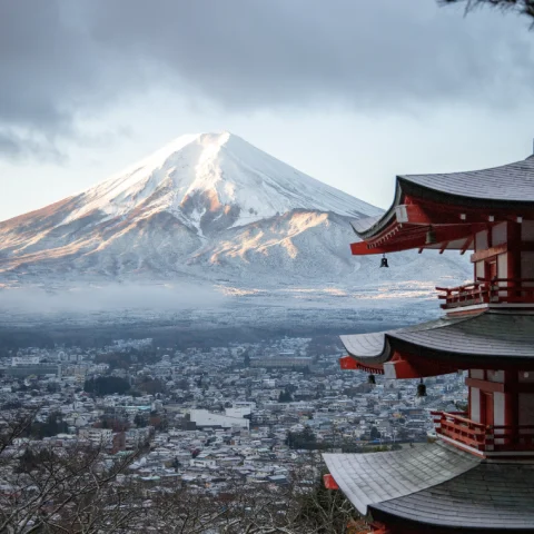 A view of an ancient red temple and Mount Fuji in the background. 
