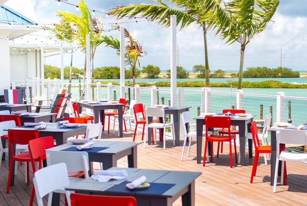 white, red, and lack chairs on a deck overlooking ocean with palm trees