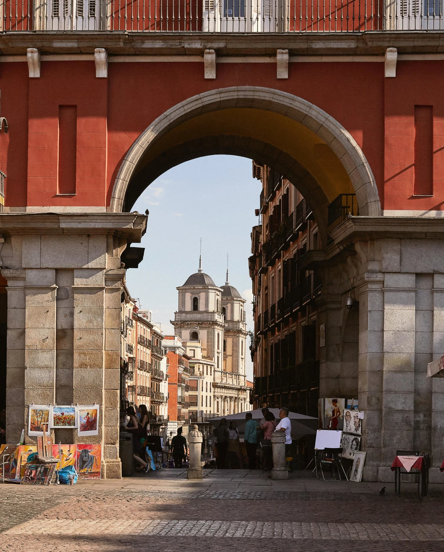a large archway leads into a narrow city street with vendors and artists