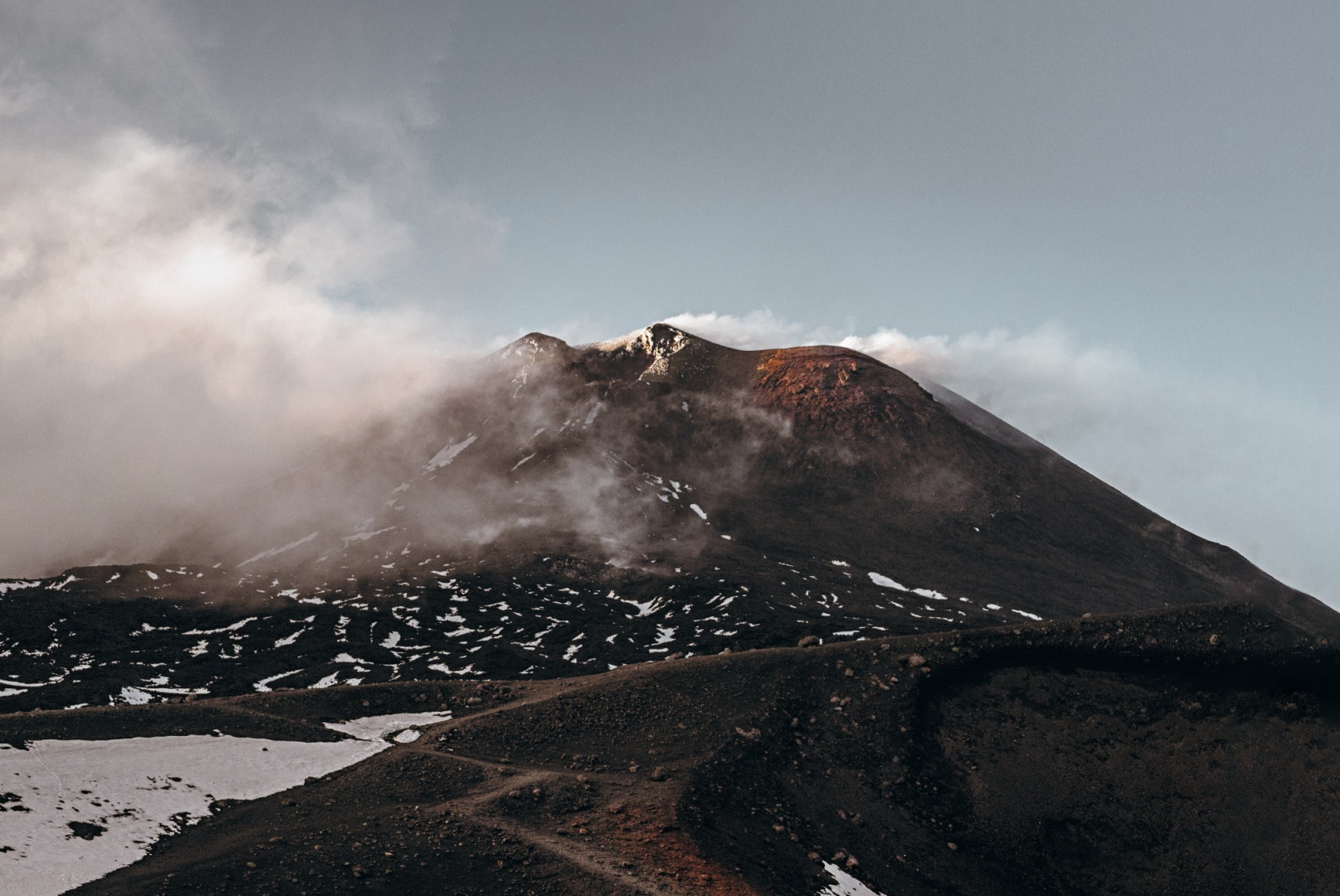 slightly snow-capped Mount Etna partially covered by clouds