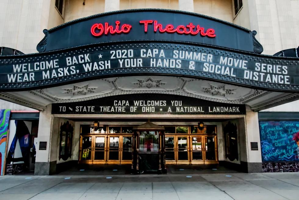 Large black sign with red and white writing above gold doors during daytime