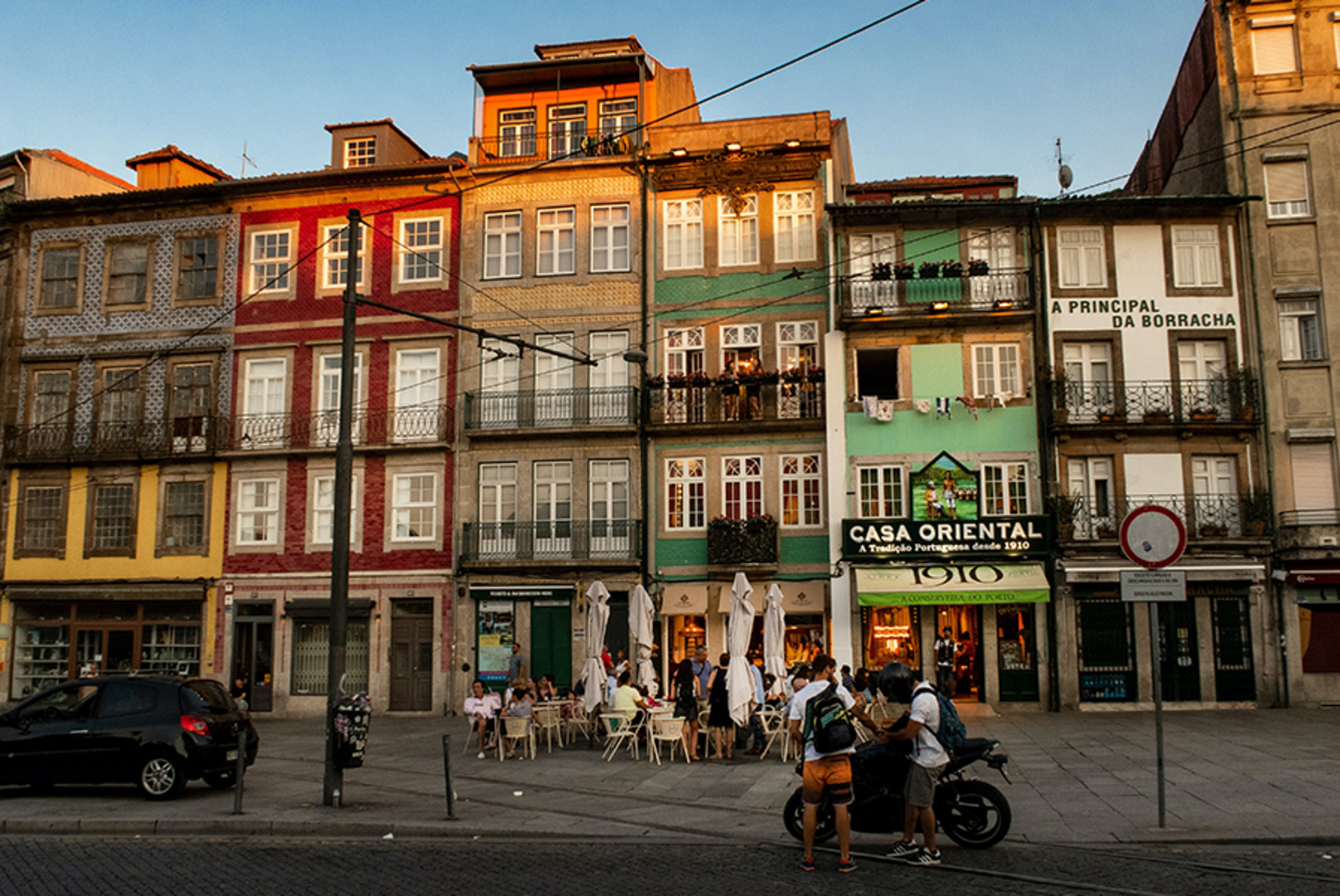 Buildings in Porto Portugal with red and green paint people out front eating with white umbrellas at sunset