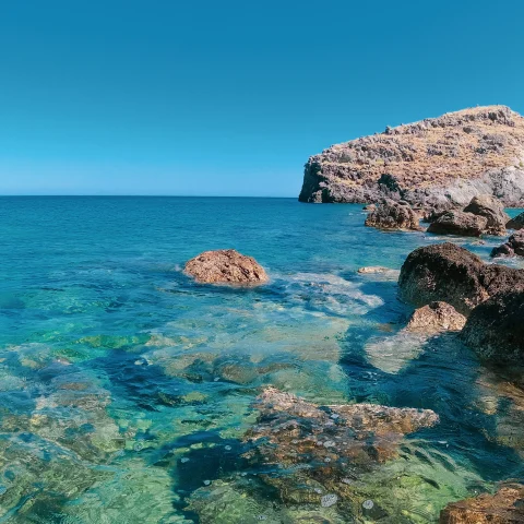 blue clear water with tan rocks and blue sky in Crete