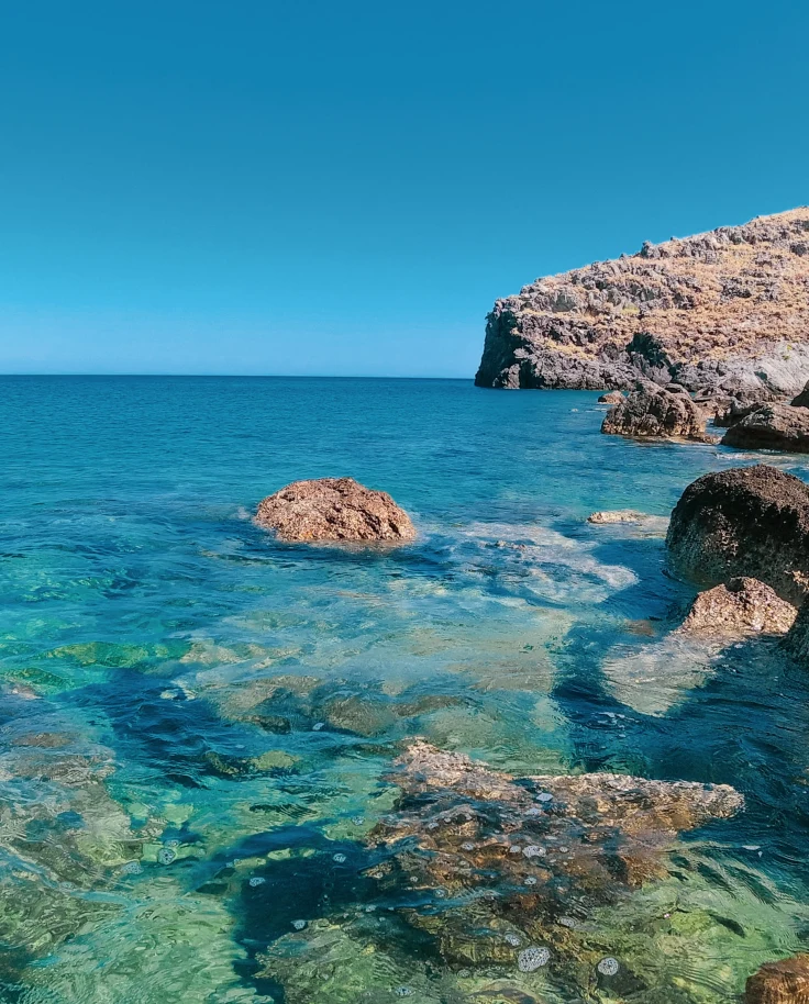 blue clear water with tan rocks and blue sky in Crete