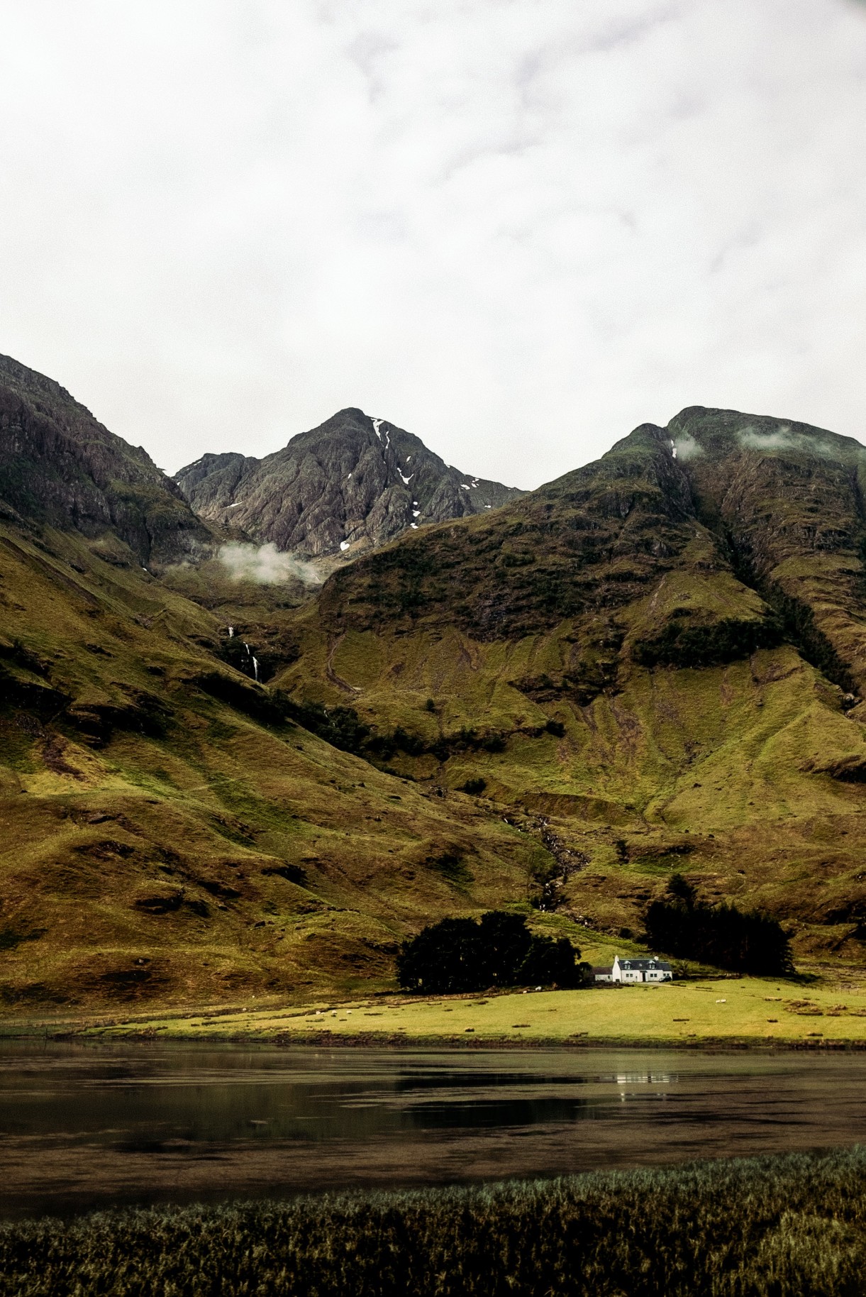 Green pastures with a small house and lake in Scotland. 