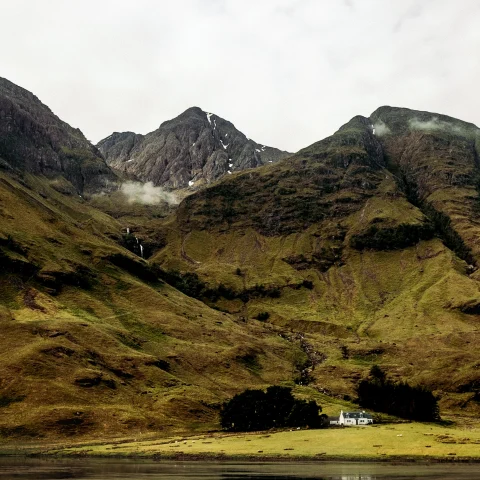 Green pastures with a small house and lake in Scotland. 