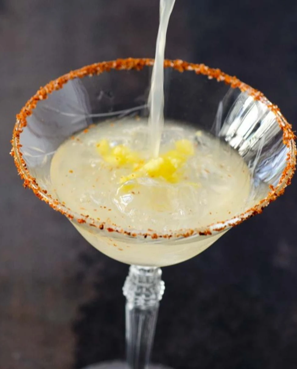 Delicious margaritas being poured in a coup glass with a spicy salt rim. 