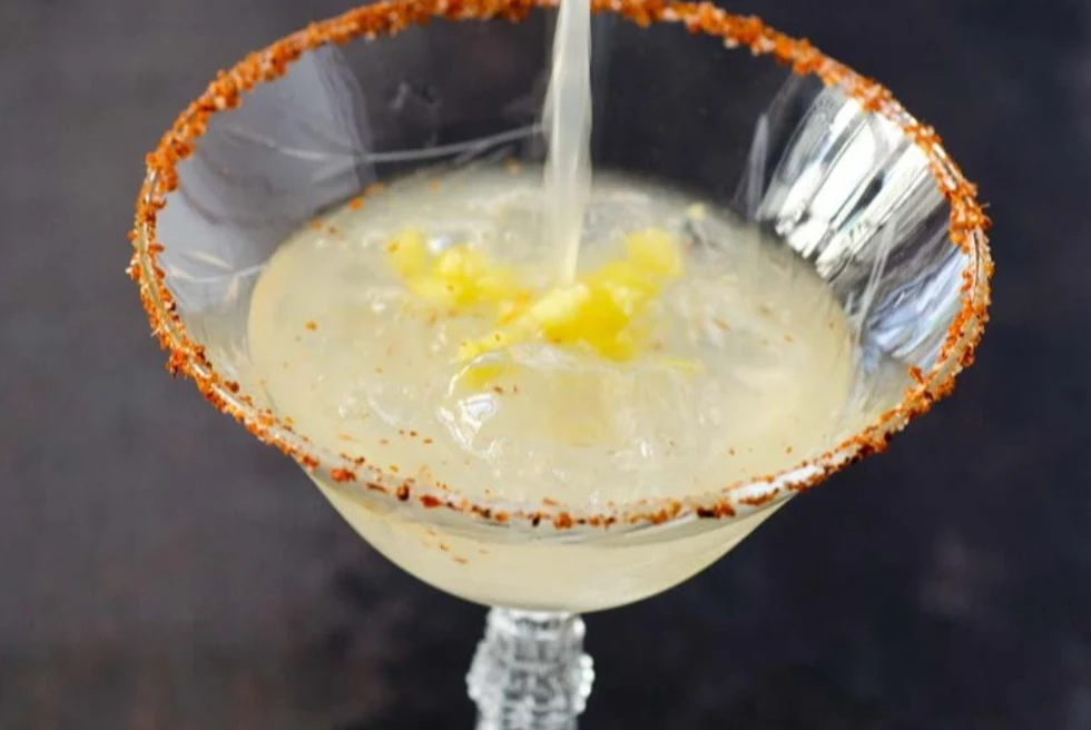 Delicious margaritas being poured in a coup glass with a spicy salt rim.