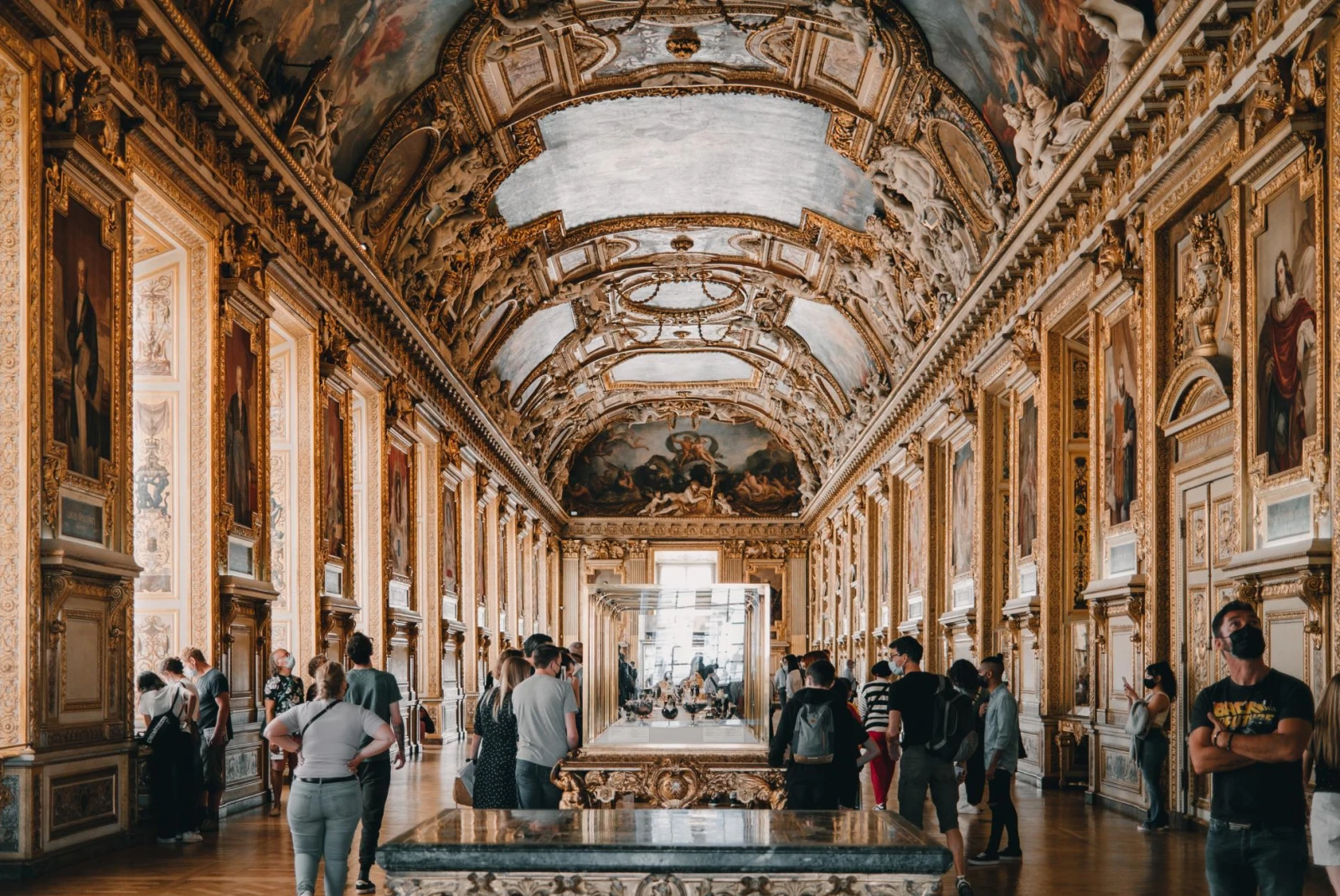 Inside a decorated hall of the Louvre displaying Renaissance paintings from floor to ceiling.