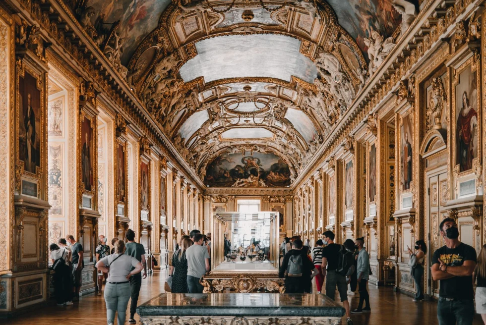 Inside a decorated hall of the Louvre displaying Renaissance paintings from floor to ceiling.