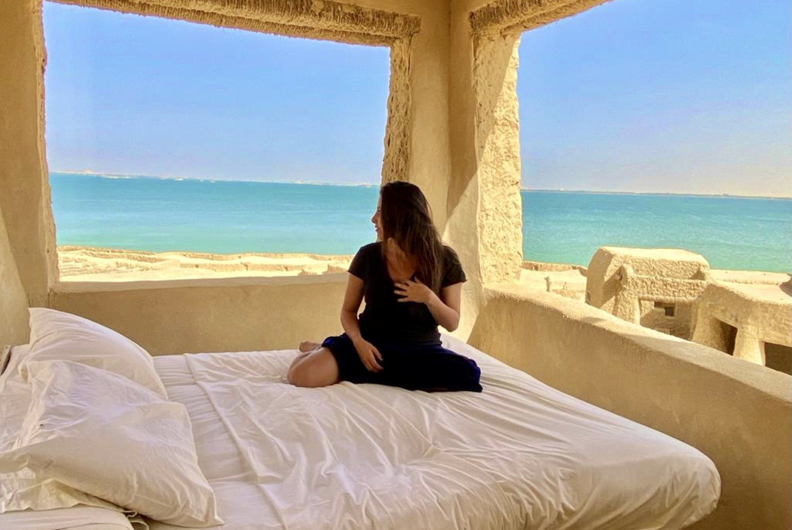 woman on white bed with body of water in the background