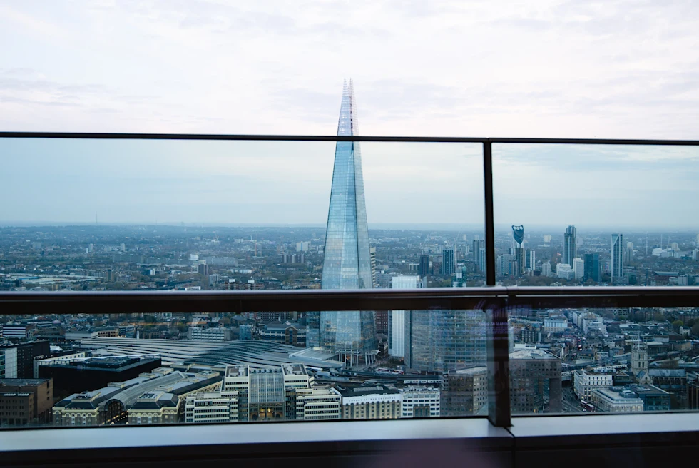 Railing and glass windows overlooking tall pointed building on a cloudy day