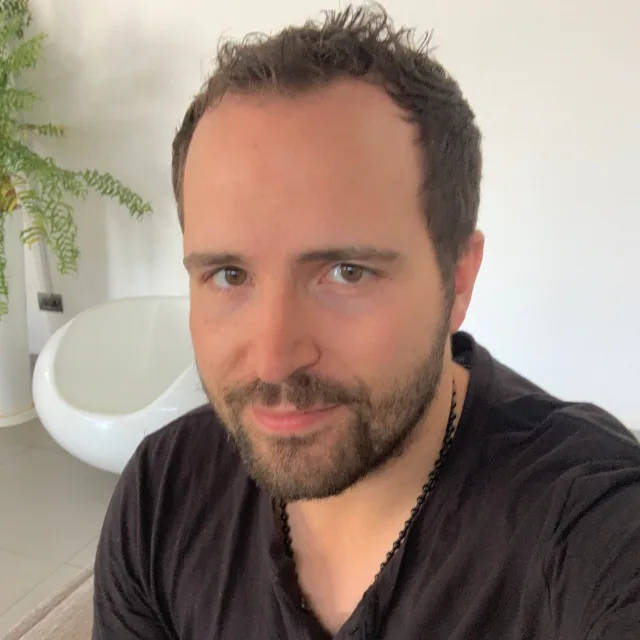 Travel Advisor Colin Howard with a black shirt in front of a white wall and furniture/green plant.