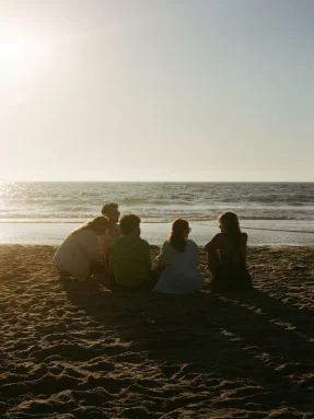 group of people sitting on a beach during sunrise