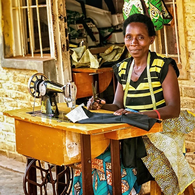 woman sitting at sowing machine station in Rwanda Africa yellow brick walls and wooden desk
