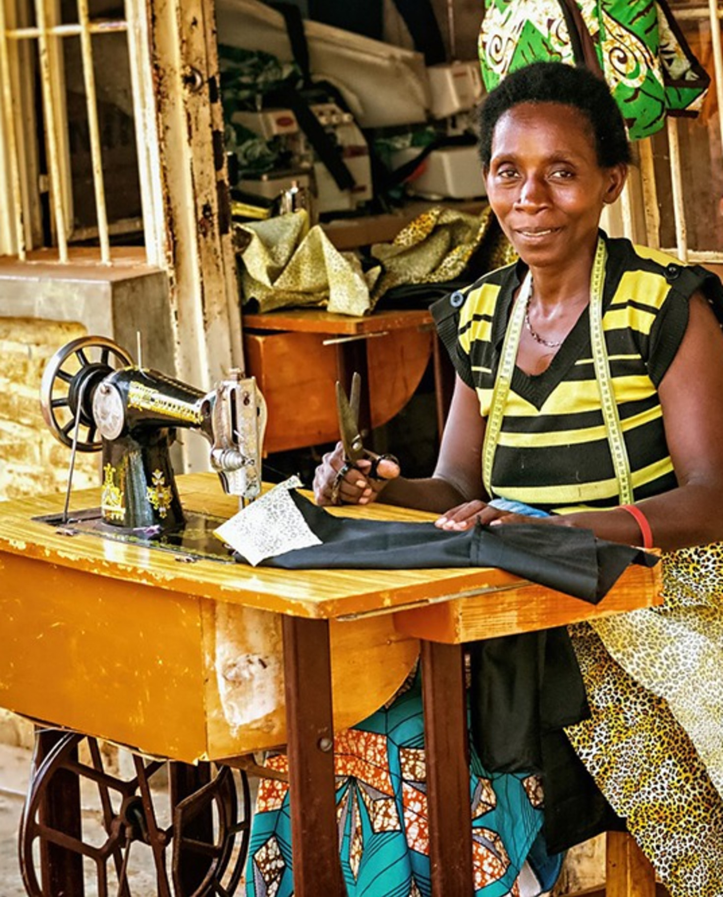 woman sitting at sowing machine station in Rwanda Africa yellow brick walls and wooden desk