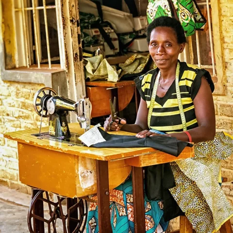 woman sitting at sowing machine station in Rwanda Africa yellow brick walls and wooden desk