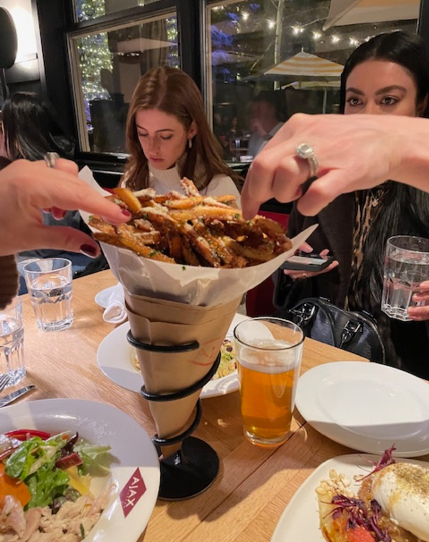 A group of people reaching for French fries in the center of a table.