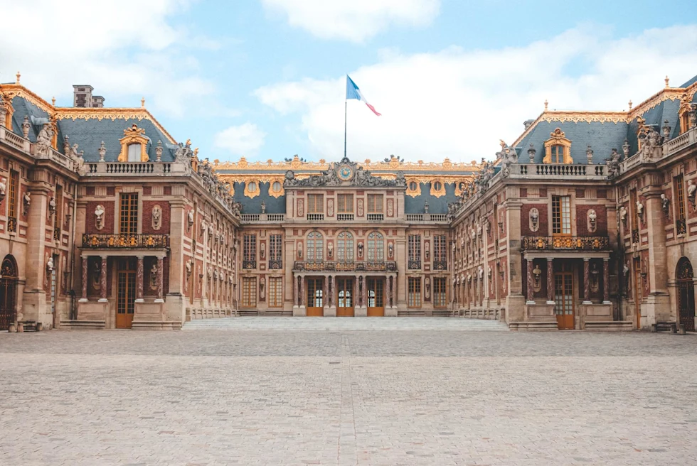 entrance to an ornate castle with the french flag flying above