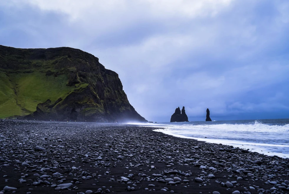 black sand beach contrasted with white ocean waves on the shore with mountains in the distance
